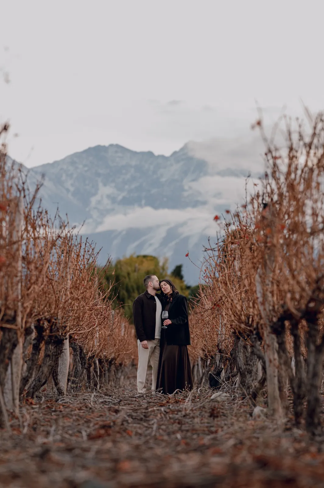 Pareja en un camino de viñedos bajo las montañas nevadas