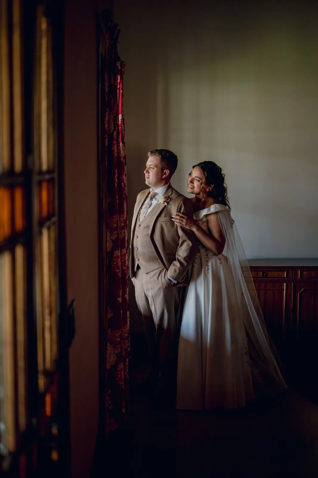 Novios abrazados junto a una ventana, con luz cálida