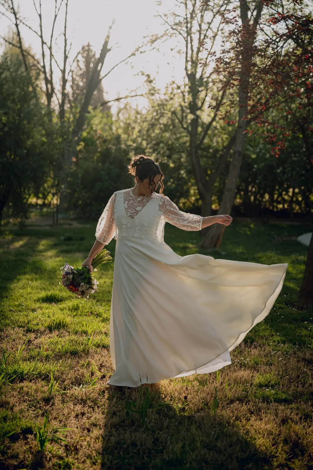 Novia girando su vestido sobre el césped con luz de atardecer
