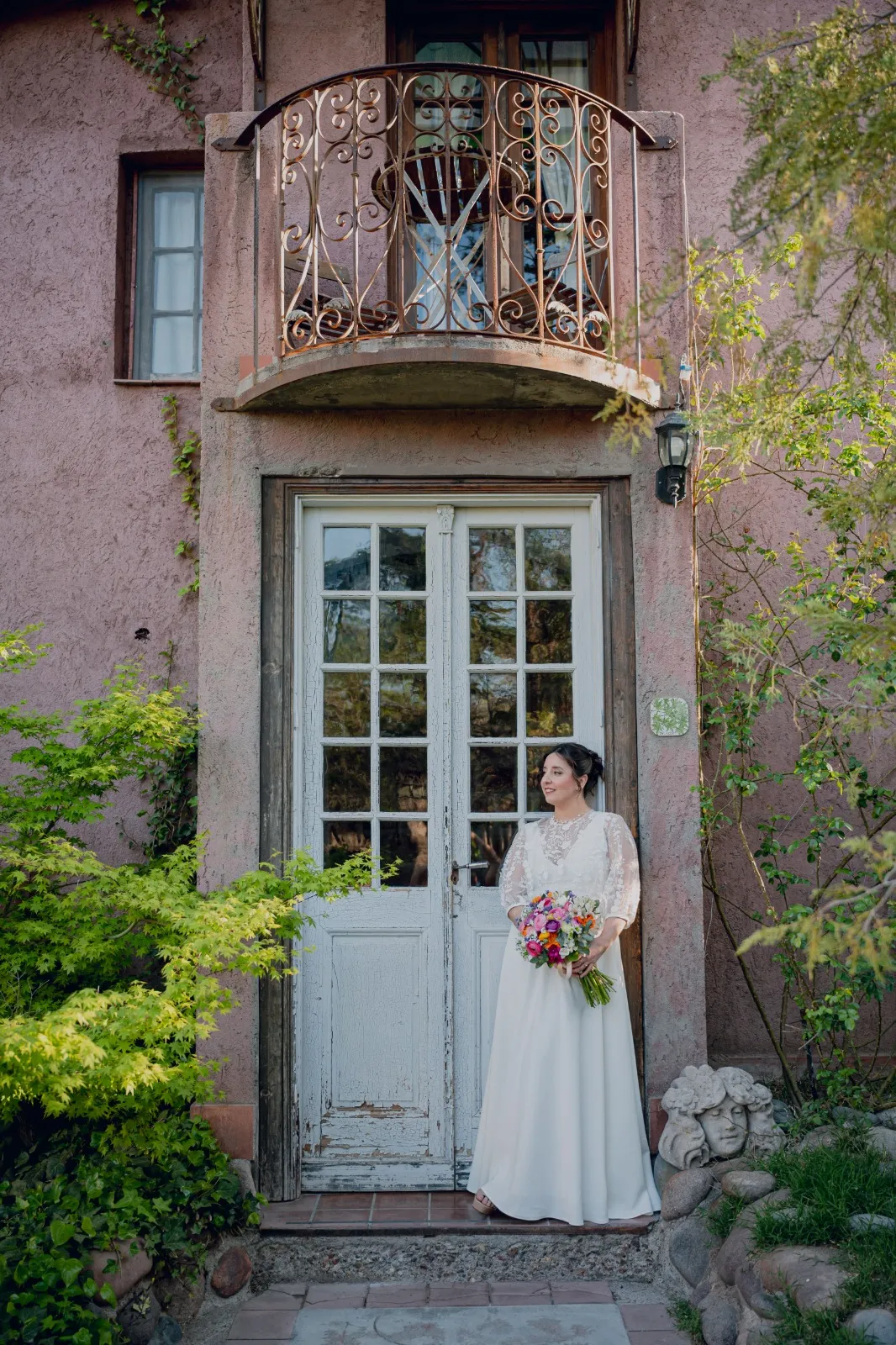 Novia con su ramo junto a una puerta antigua con balcón