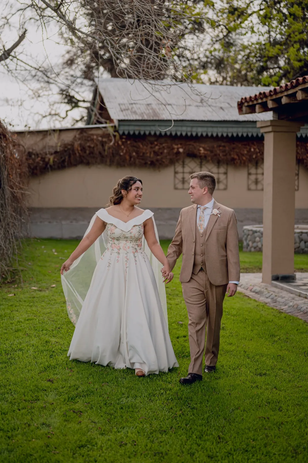 Novios caminando de la mano frente a una casa de campo