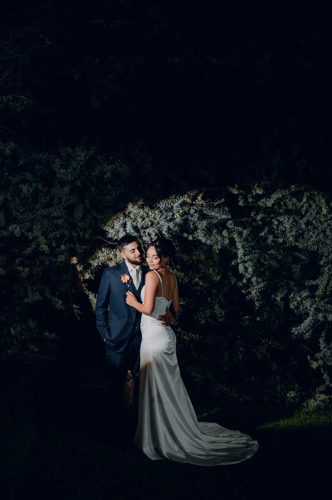 Pareja de noche junto a un arbusto iluminado