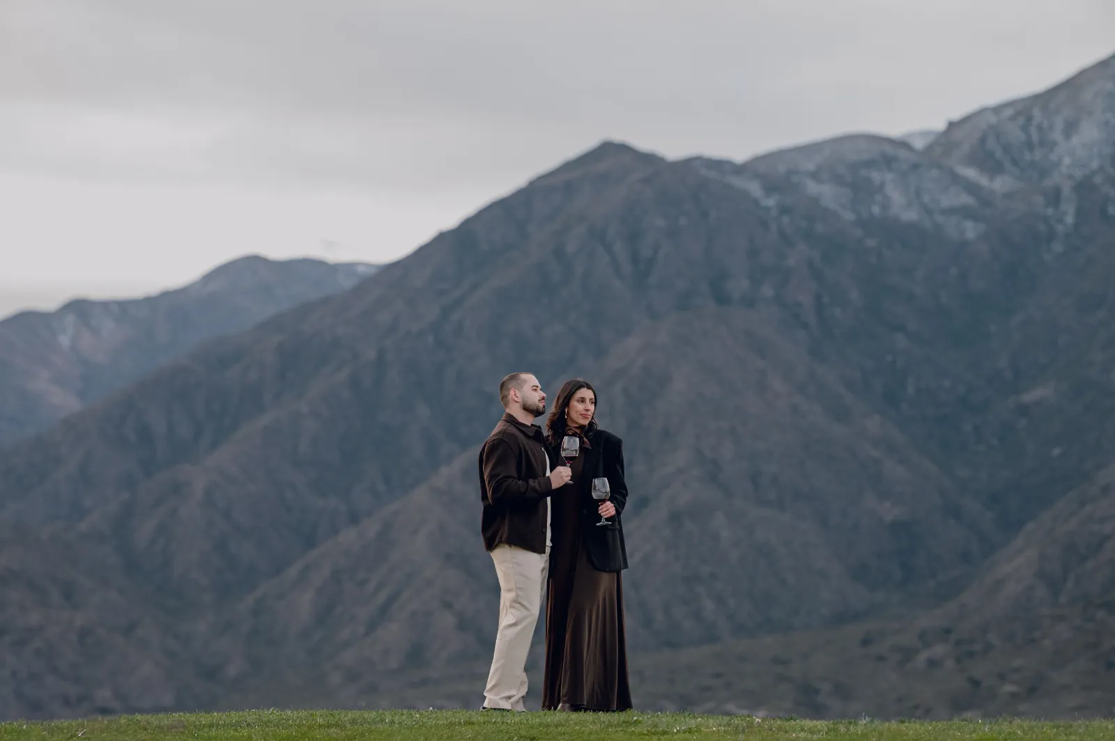 Pareja de pie frente a las montañas bajo un cielo nublado